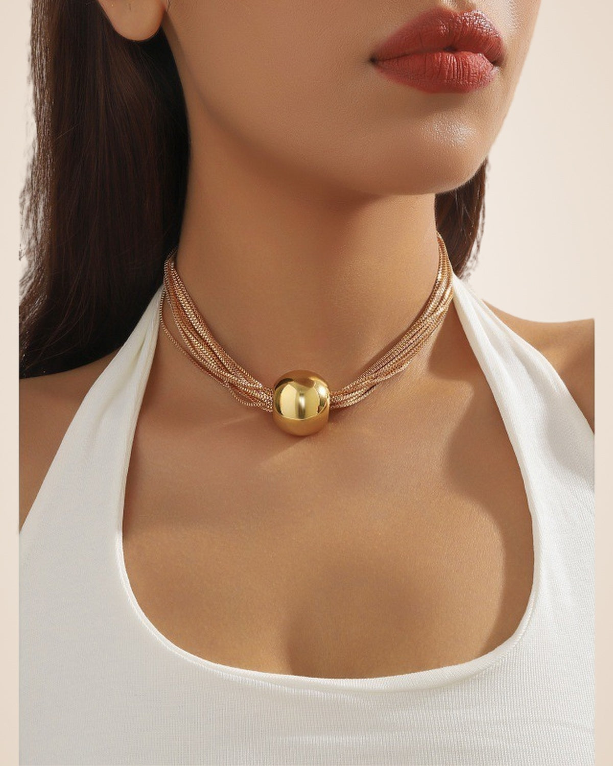 Collier court multirang à boule dorée porté avec un haut dos nu blanc
